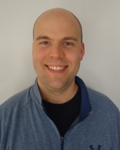 Headshot of a white man smiling in front of a gray backgorund